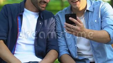 两个朋友坐在公园的长凳上看智能手机上的<strong>搞笑视频</strong>，特写镜头